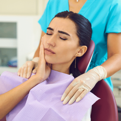 When should you visit an emergency dentist? 11 A woman in a dentist chair holding her jaw in pain, representing emergency dentist